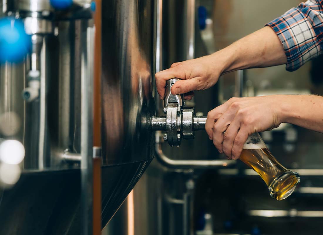 Brewery Insurance - Close-up of a Local Brewer Owner Filling up Beer in a Tall Glass from the Tank at a Small Brewery
