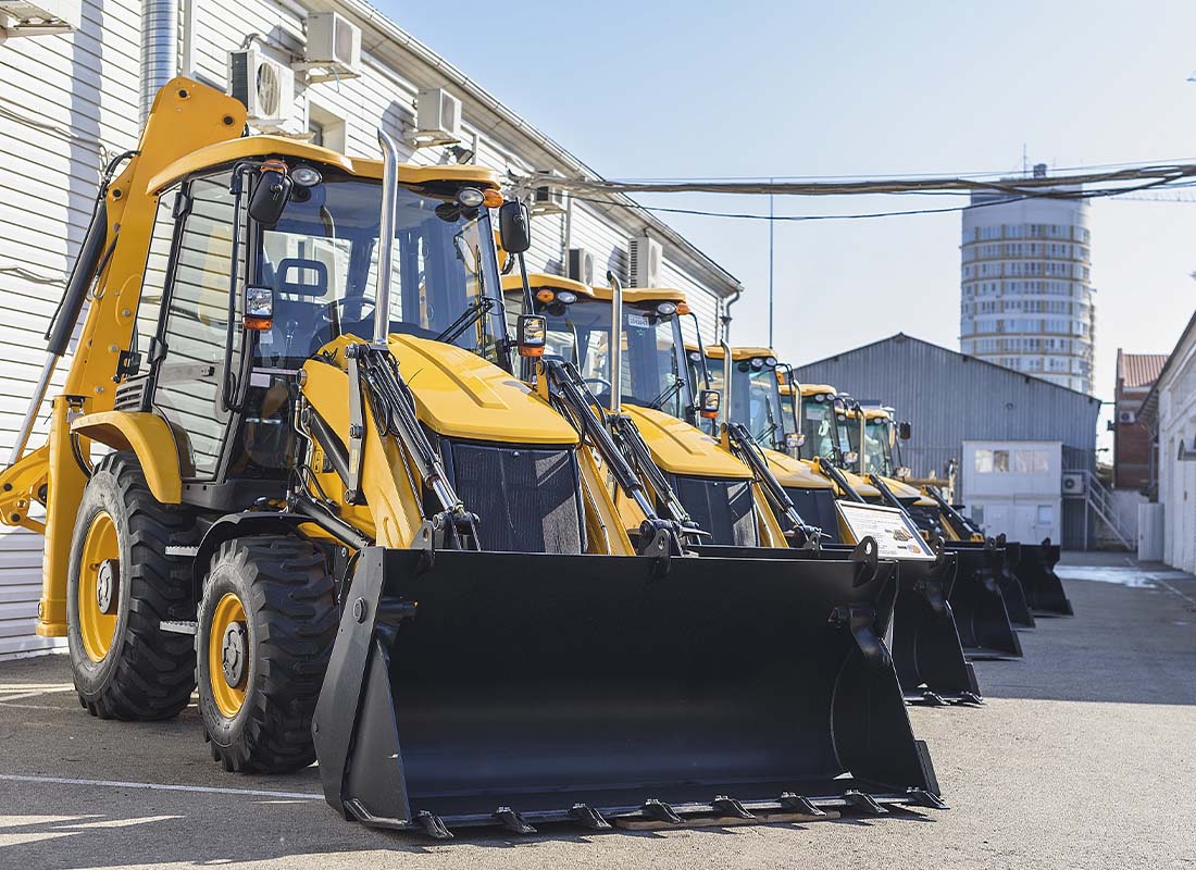Equipment Rental Insurance - Row of Construction Equipment Displayed for Rental Use Behind a Warehouse on a Sunny Day