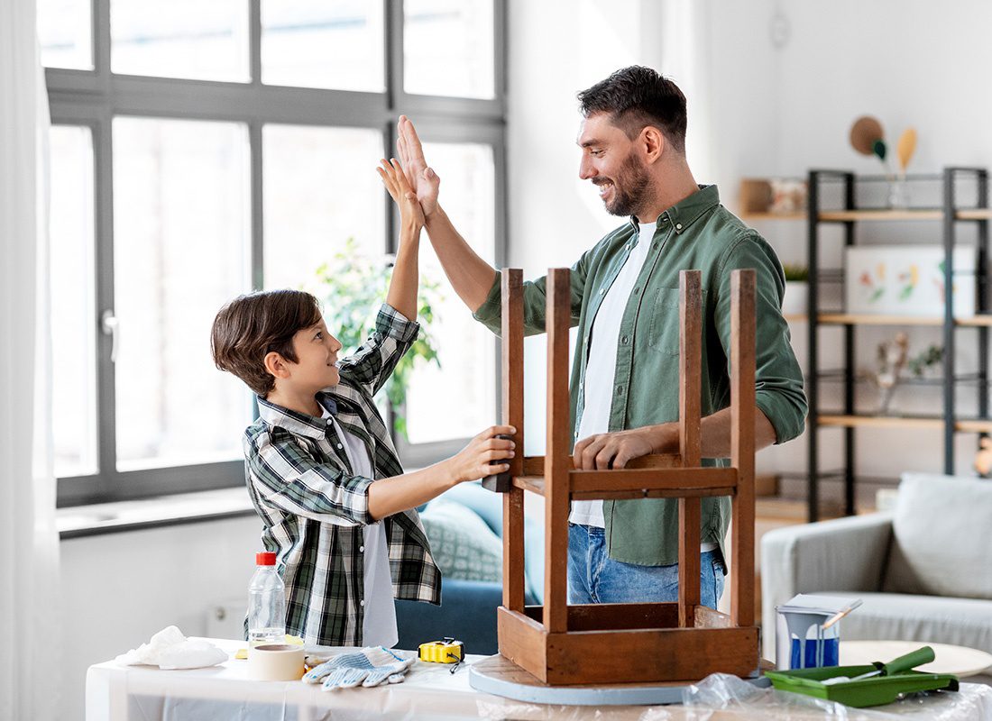 Personal Insurance - Father and Son Celebrate as They Work on Finishing a Small Wooden Table in Their Home
